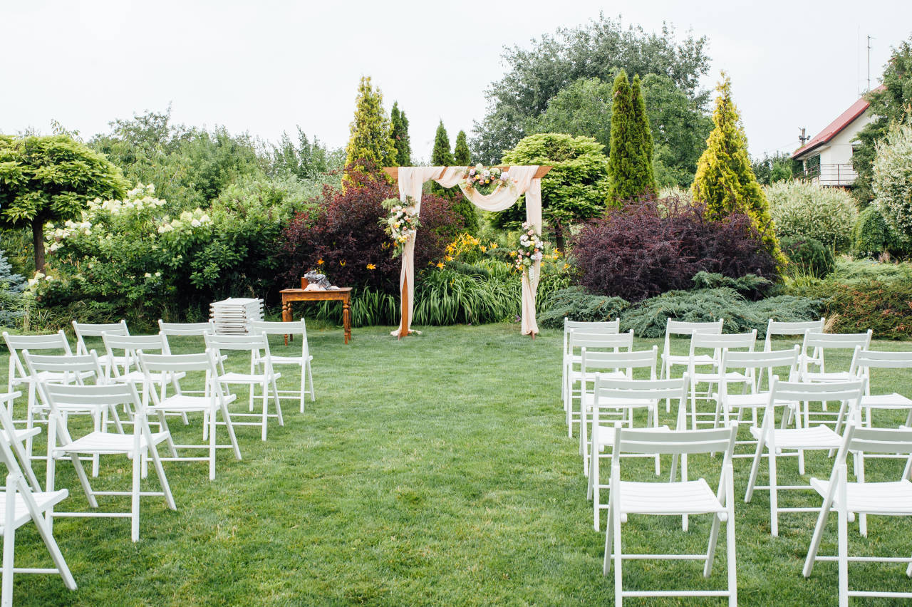 hochzeitsrausch Brautmoden - Freie Trauung im Garten mit elegantem Blumenbogen und weißen Stühlen, romantische Hochzeitsatmosphäre