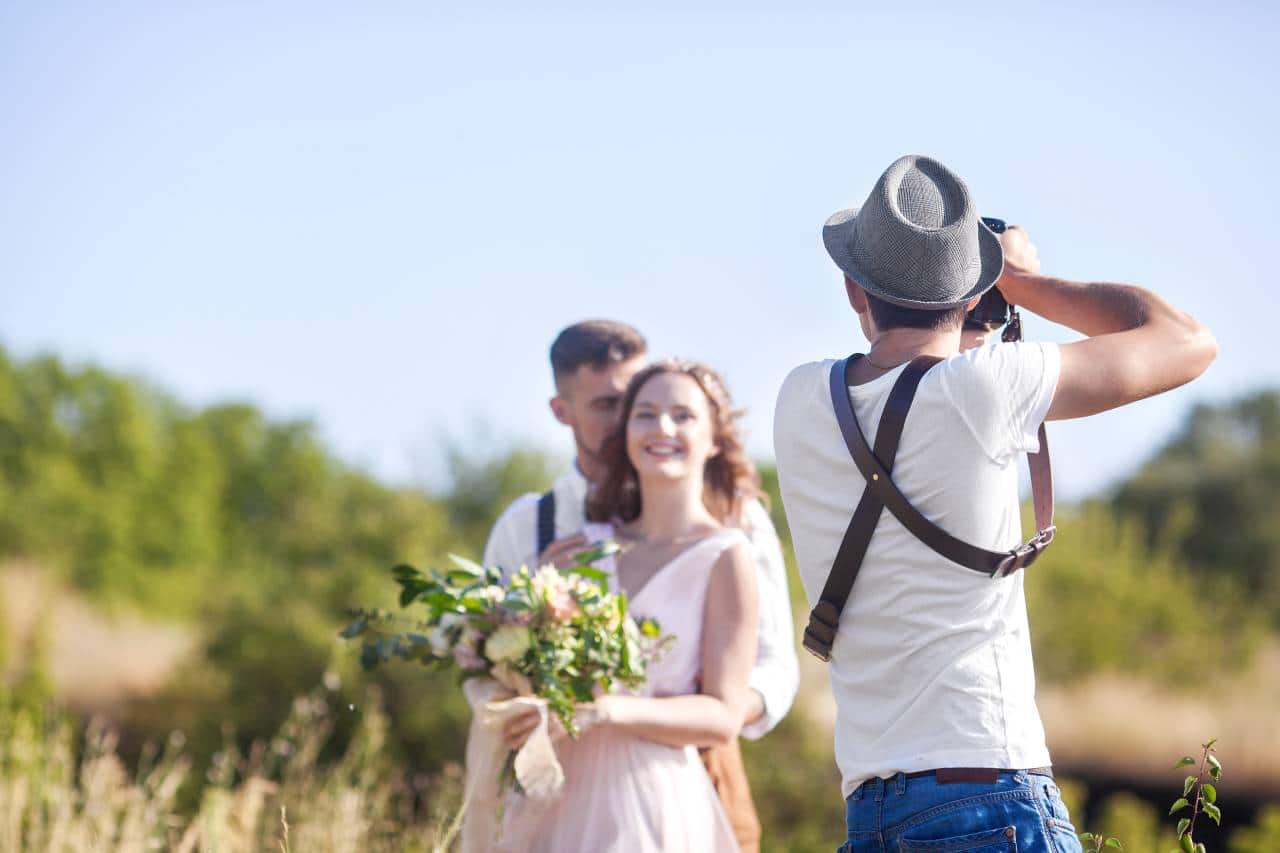 hochzeitsrausch Brautmoden - Fotograf bei Outdoor-Hochzeitsshooting, Brautpaar mit Blumenstrauß im Fokus