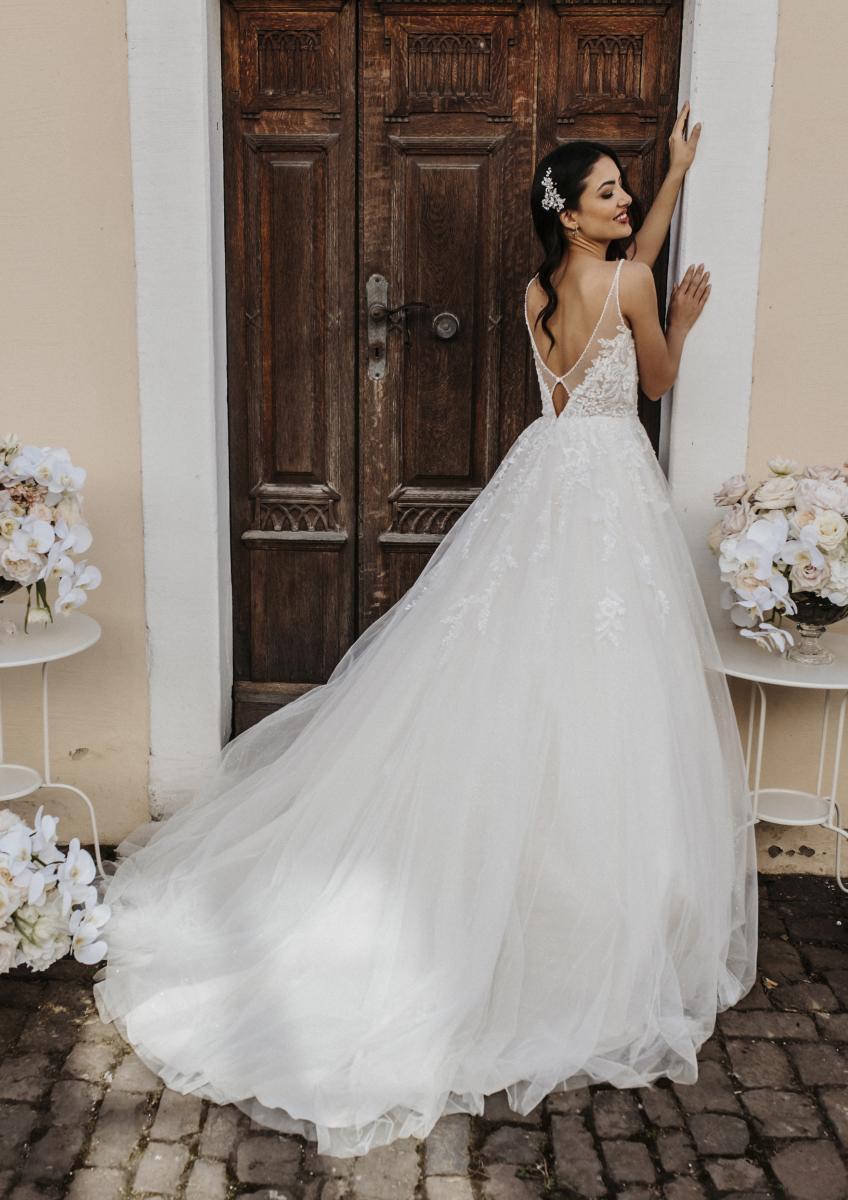 hochzeitsrausch Brautmoden - Elegantes Brautkleid mit Spitzenrücken und Tüllrock vor rustikaler Holztür
