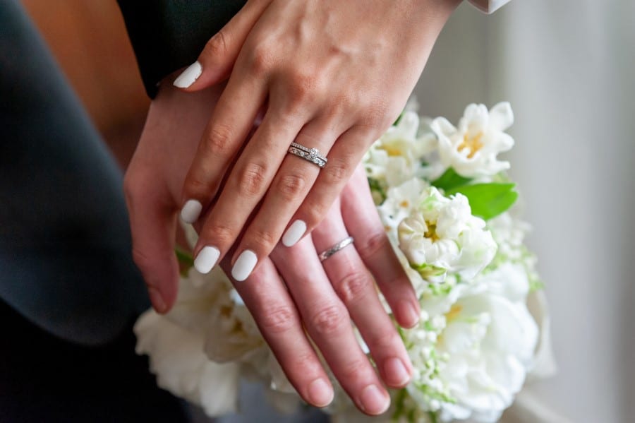 hochzeitsrausch Brautmoden - Eheringe auf Haenden mit Blumenstrauss, symbolisch fuer Hochzeit und Liebe
