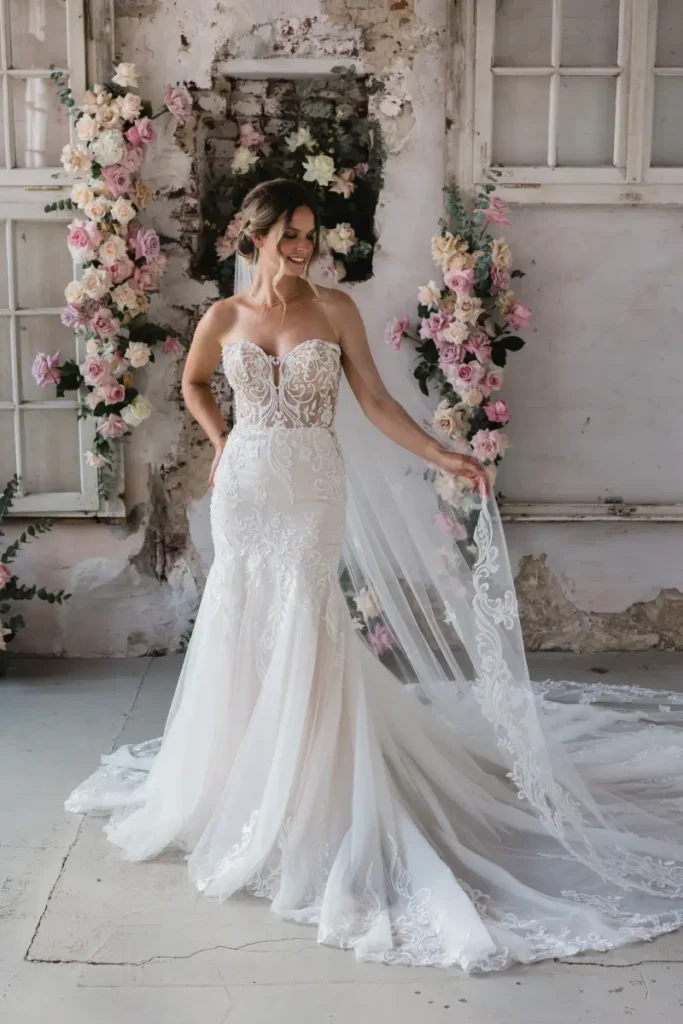 hochzeitsrausch Brautmoden - Elegantes Brautkleid mit Spitzen und Schleppe vor romantischem Blumenhintergrund