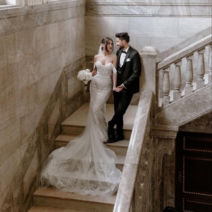 hochzeitsrausch Brautmoden - Elegantes Brautkleid mit Spitzen und langer Schleppe, Brautpaar auf Marmortreppe
