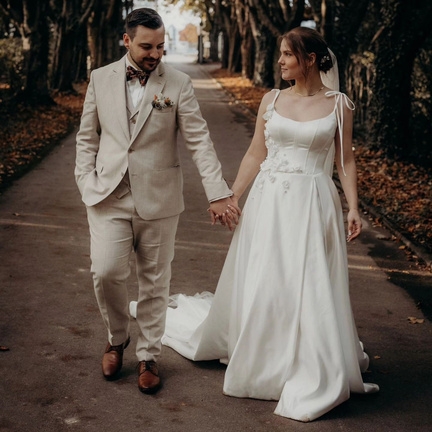 hochzeitsrausch Brautmoden - Brautkleid mit floralen Details und eleganter Bräutigam-Anzug in herbstlicher Allee