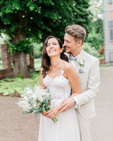 hochzeitsrausch Brautmoden - Brautkleid mit Spitzenoberteil und Braeutigam-Anzug in hellem Beige, romantische Gartenkulisse