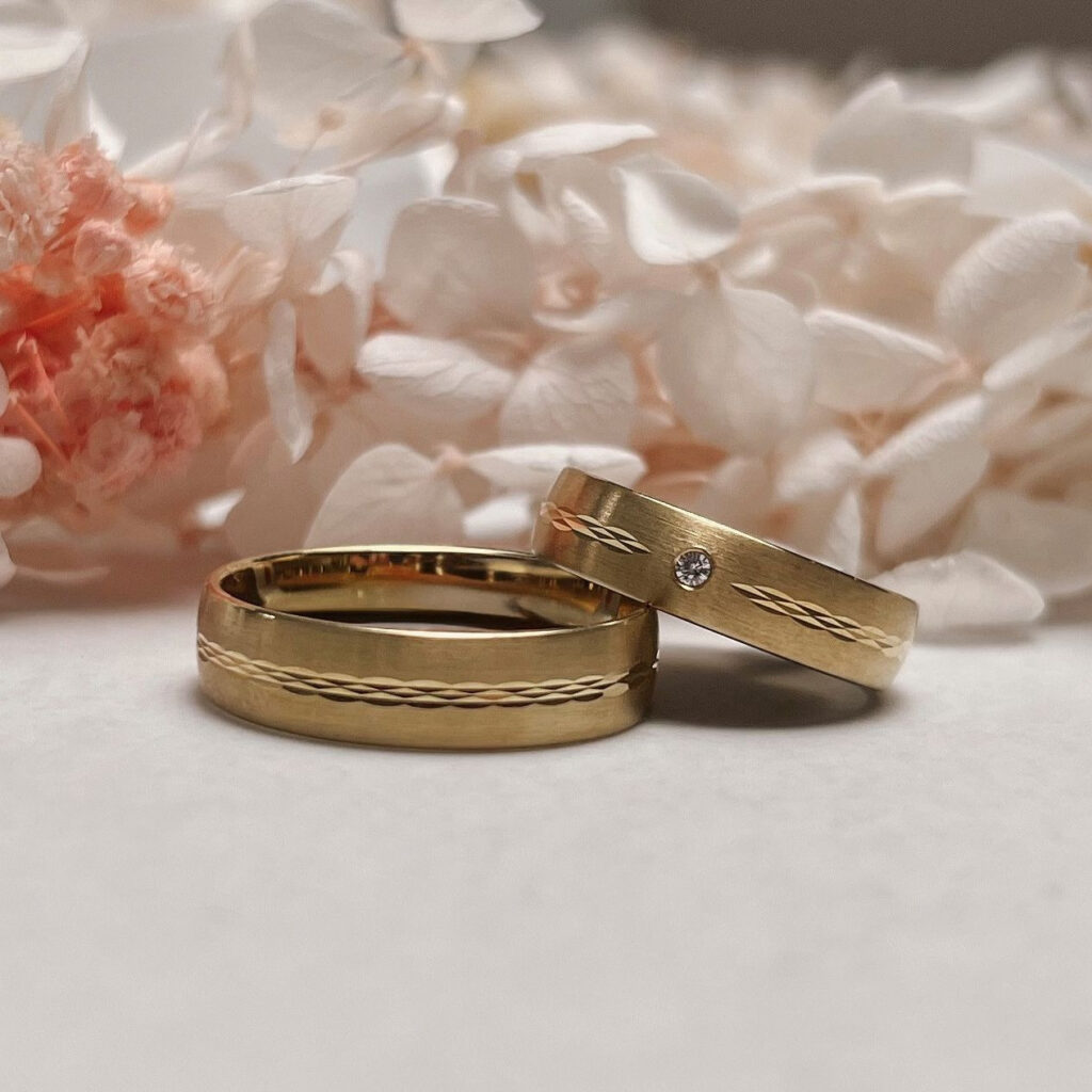 hochzeitsrausch Trauringe in Gold mit Diamant-Detail, umgeben von zarten weißen Blüten, elegant und zeitlos