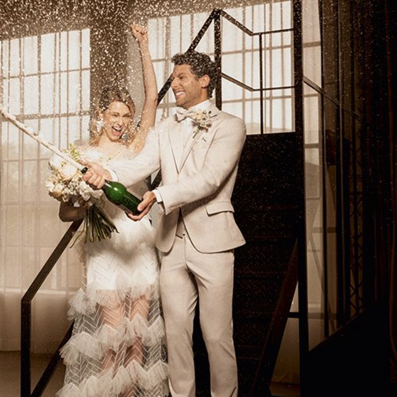 hochzeitsrausch Brautmoden - Atelier Torino Vintage Hochzeitsanzug im Boho-Stil, Brautpaar feiert mit Champagner