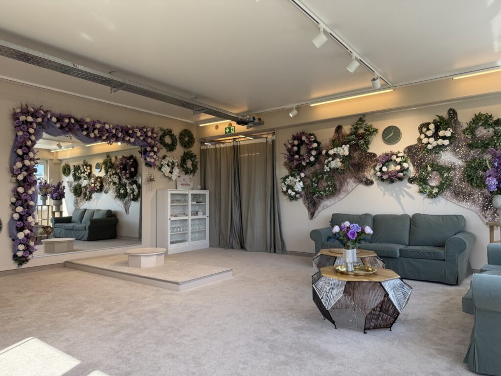 Eine stilvolle Lounge mit hellem Teppich, blauen Sofas und verspiegeltem Couchtisch dient als hochzeitsrausch Brautmoden Berlin Schönefeld Anprobezimmer, mit lila Blumenarrangements und eleganten Spiegeln für eine gemütliche, sanft beleuchtete Atmosphäre.