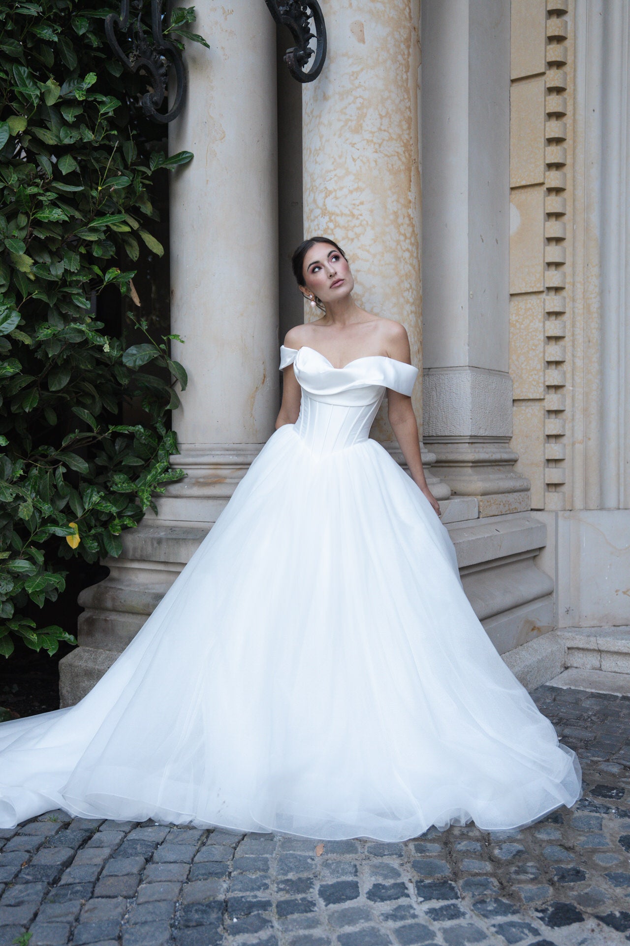 hochzeitsrausch Brautmoden - Elegantes Brautkleid mit schulterfreiem Design und voluminösem Rock vor klassischer Kulisse