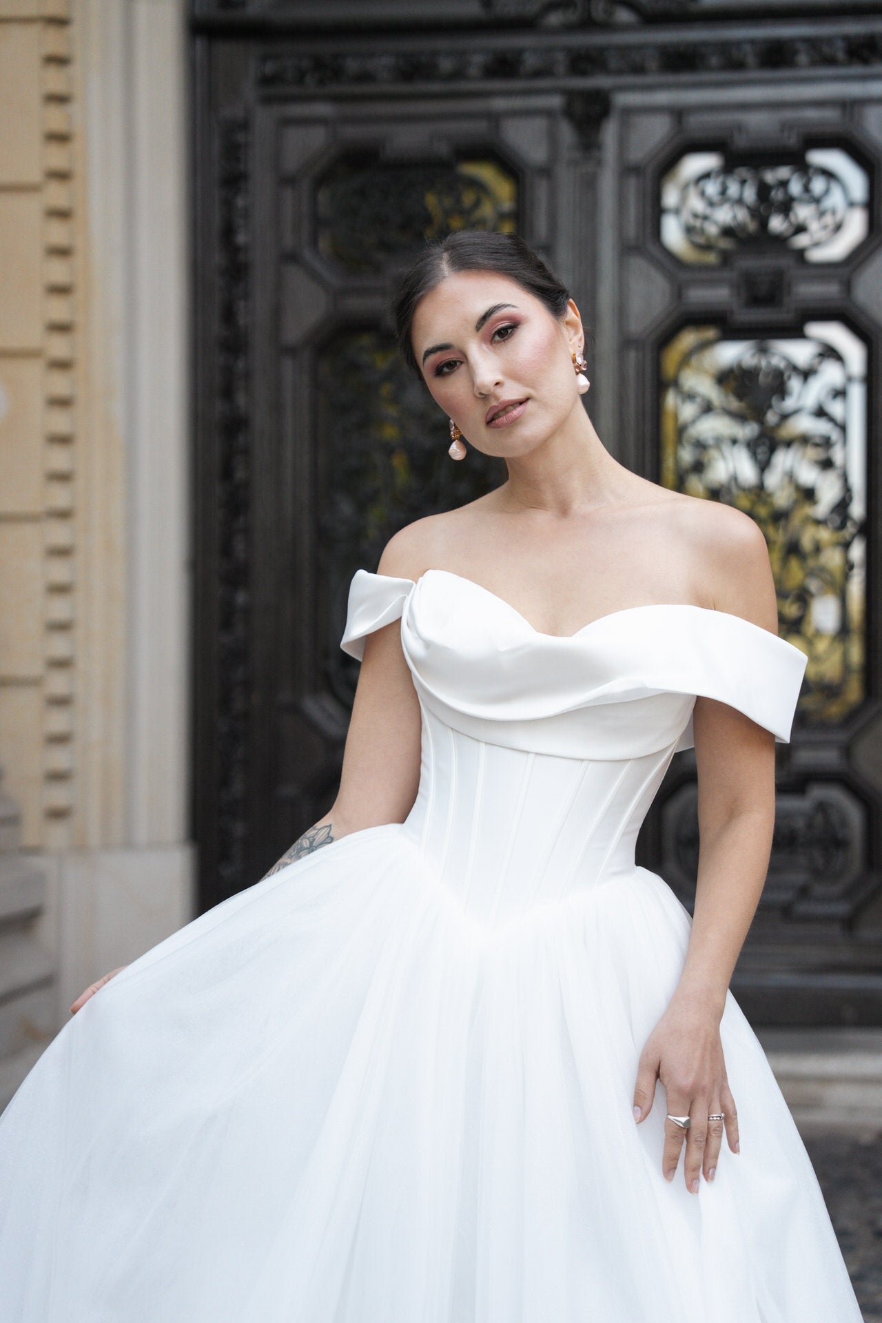 hochzeitsrausch Brautmoden - Elegantes Brautkleid mit schulterfreiem Design und voluminösem Rock vor historischer Tür
