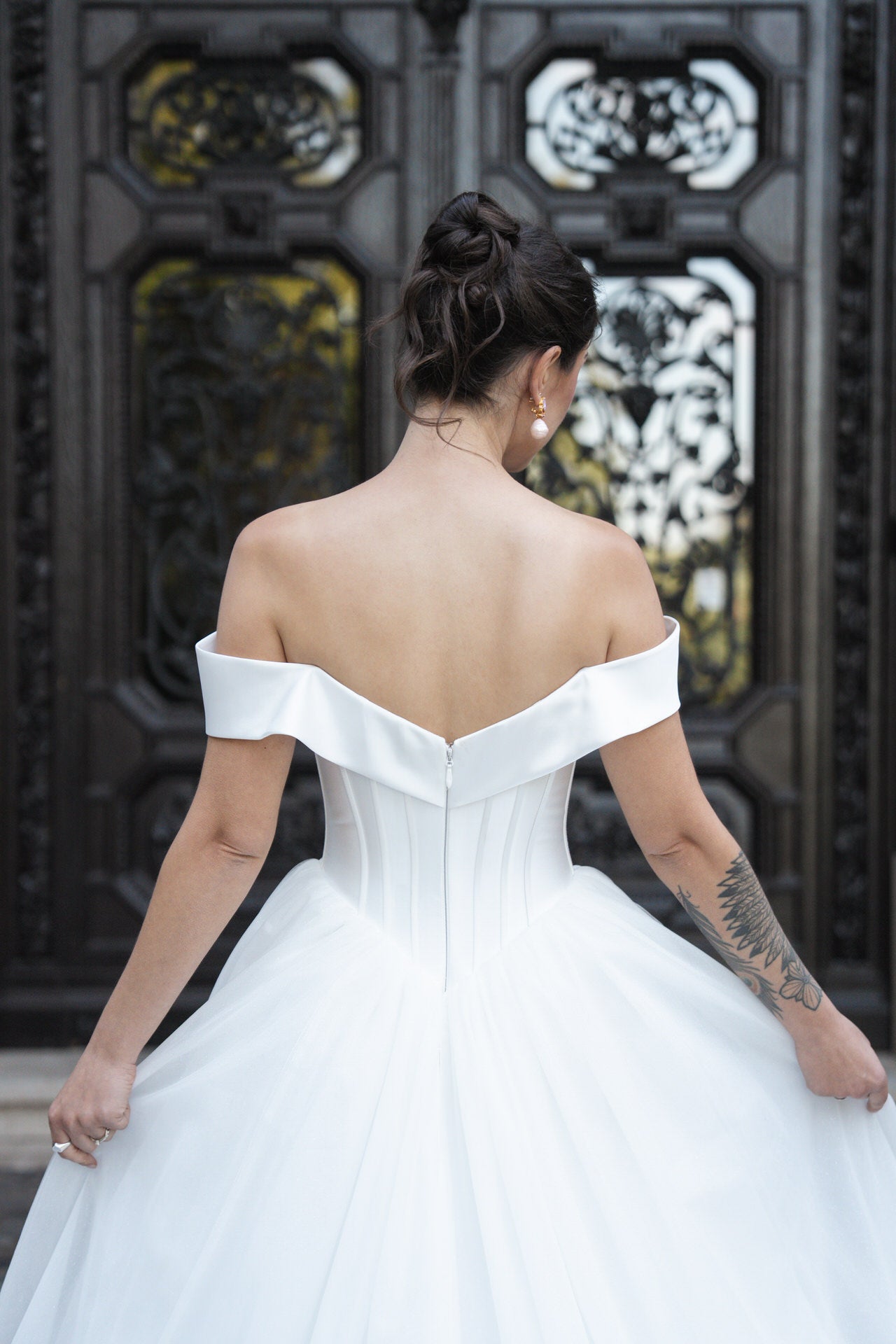 hochzeitsrausch Brautmoden - Elegantes Brautkleid mit schulterfreiem Design und voluminösem Rock vor kunstvoller Tür