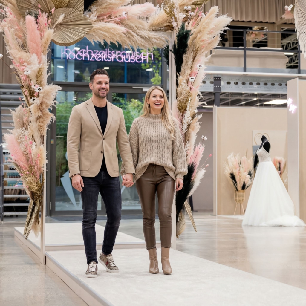 hochzeitsrausch Brautmoden - Paar im Hochzeitshaus, elegante Herbstmode, Brautkleid im Hintergrund, stilvolle Atmosphäre